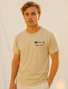 young man wearing a light tan short sleeve tee shirt with the text Cape Cod and an illustration of a fish on it