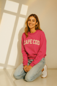 Young smiling woman wearing a raspberry rose sweatshirt with the text "Cape Cod" on it