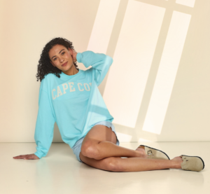 woman sitting wearing light blue sweatshirt with text Cape Code on it